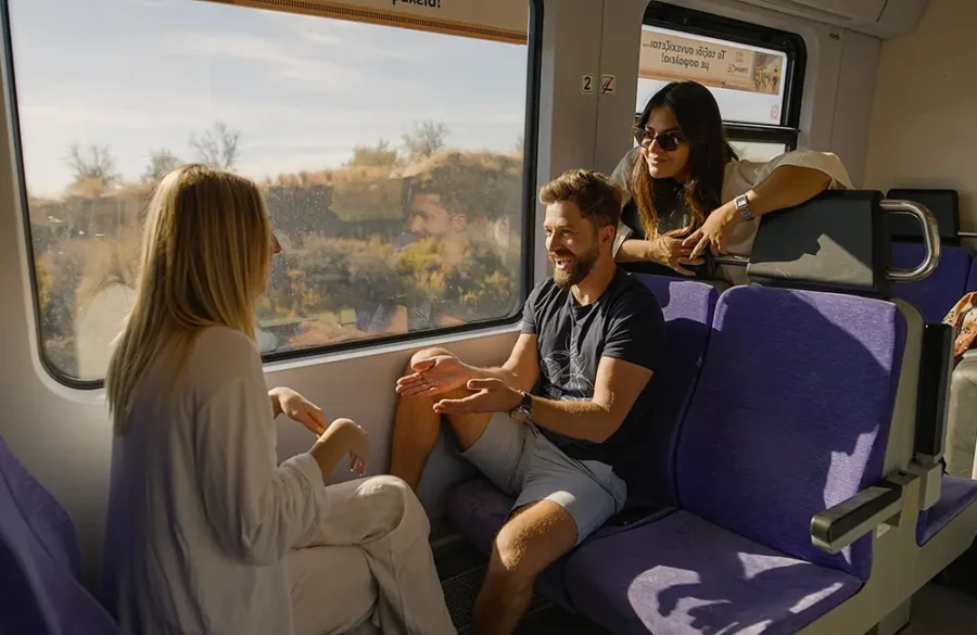 Friends enjoying a lively conversation on a scenic train journey through a sunlit rural landscape.