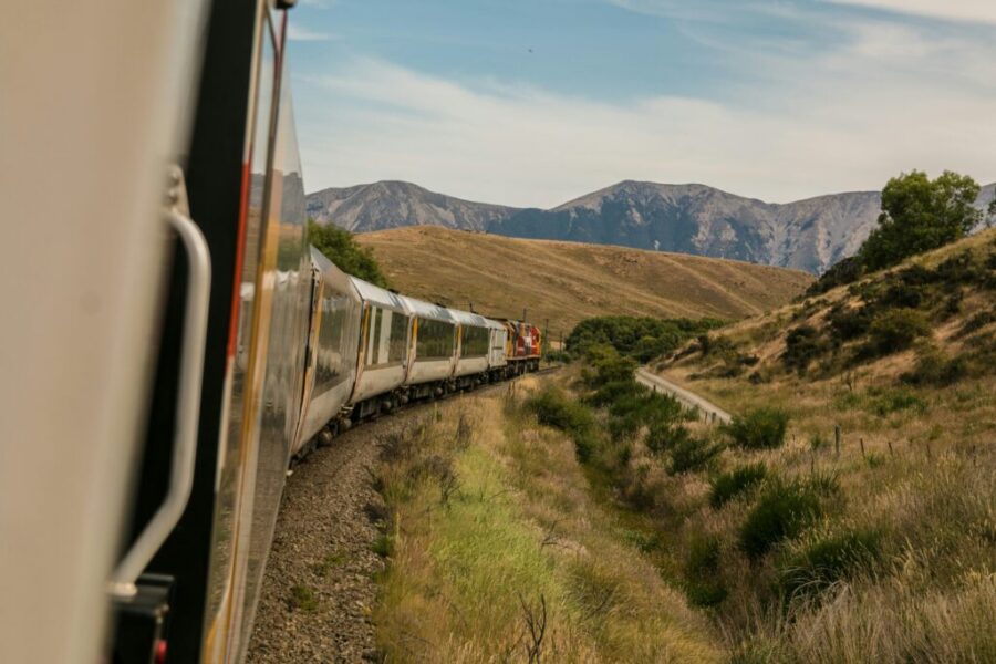 Scenic train journey through hills and mountains under a serene sky.