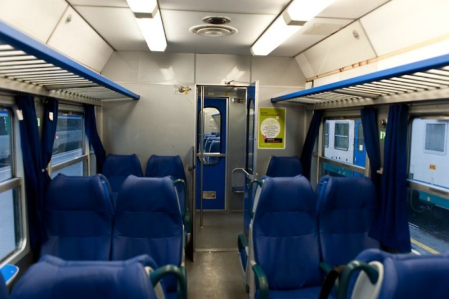 Modern train interior with blue seats, green armrests, and large windows for comfortable travel.