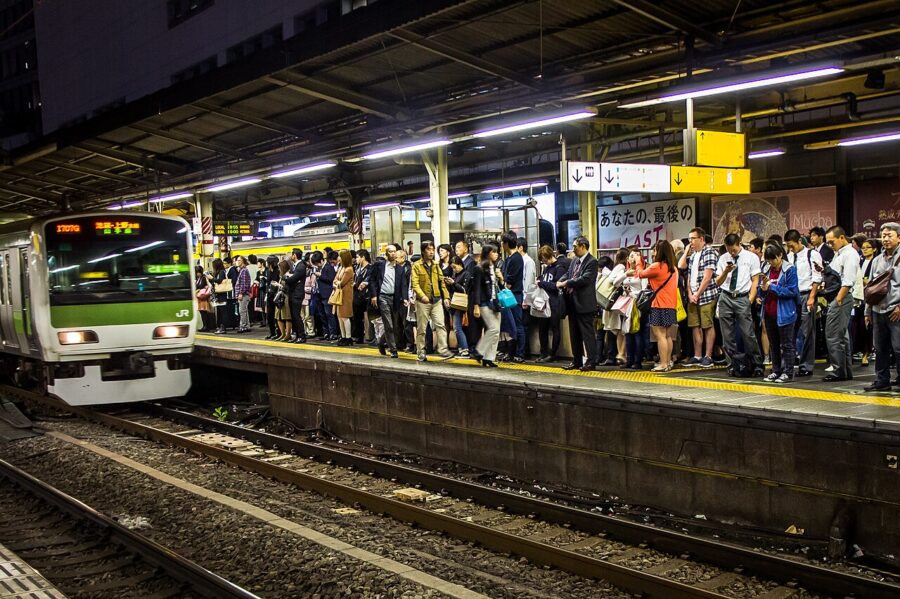 Commuters waiting on Japanese train platform as green JR train arrives during rush hour.
