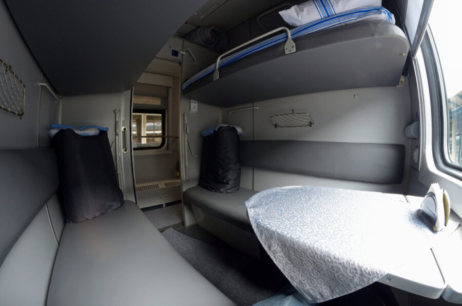First Class sleeping carriage compartment featuring a neatly made bed with linen packages ready for passengers.
