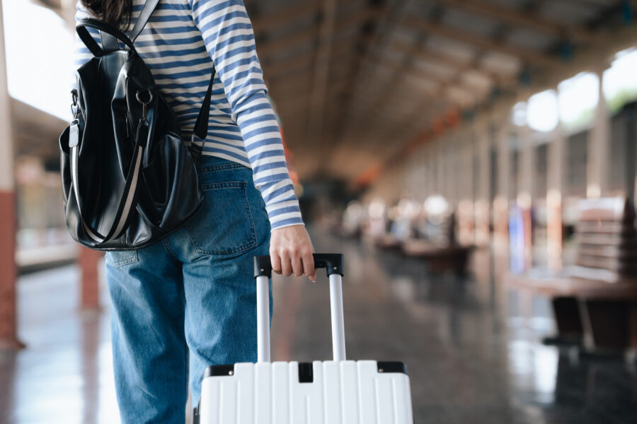 Young woman with a suitcase at a train station, traveling alone, enjoying a summer city adventure for vacation or business.
