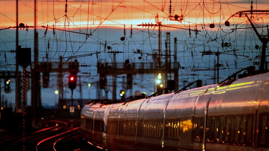 Twilight passenger train in rail yard with tracks, catenary wires, and glowing signals.