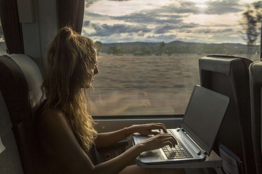 Woman working on laptop in serene train carriage with scenic landscape outside.