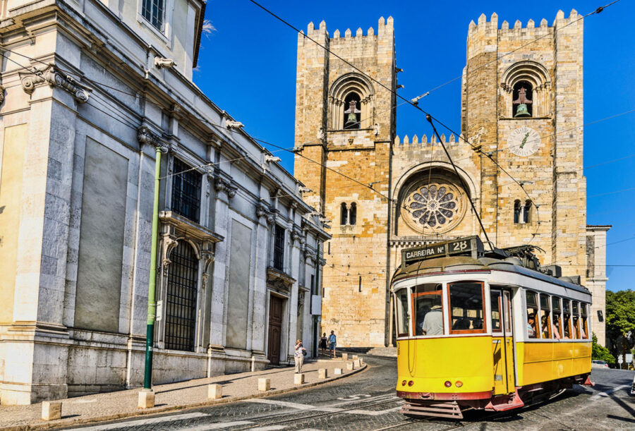 Historic Lisbon Cathedral with yellow tram on curved cobblestone street.