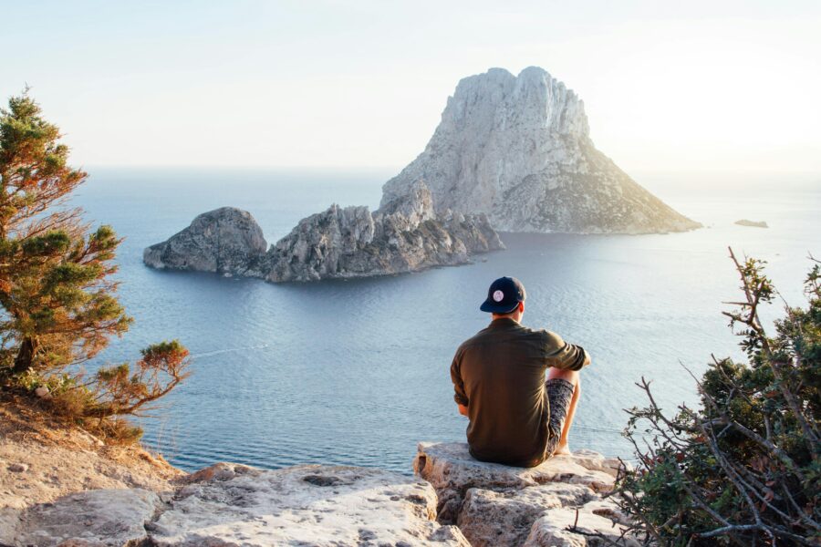 Serene coastal view with sunset, man on rocks, and shimmering water.