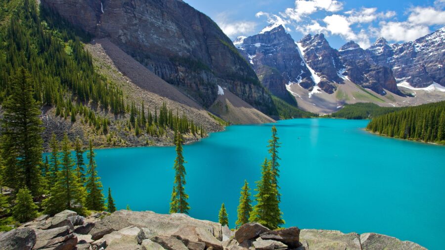 Turquoise lake with mountains, forests, and sky reflections creating a serene natural landscape.