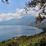 A serene lake with mountains, trees, and blue sky reflecting picturesque nature.