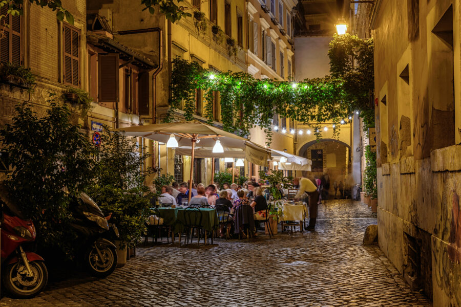 Night view of a charming old street and a restaurant in Trastevere, Rome, illuminated by warm lights and lined with historic buildings