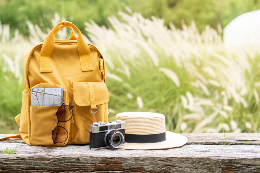 Travel backpack rests on a wooden bench, surrounded by various travel items