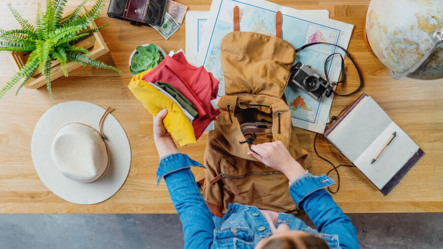Top view of a young woman arranging items in a travel bag, preparing for her upcoming vacation trip