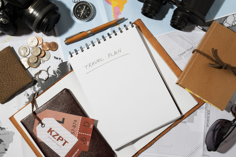 Travel planning tools: notebook, map, coins, camera, binoculars, wallet, journal, sunglasses.