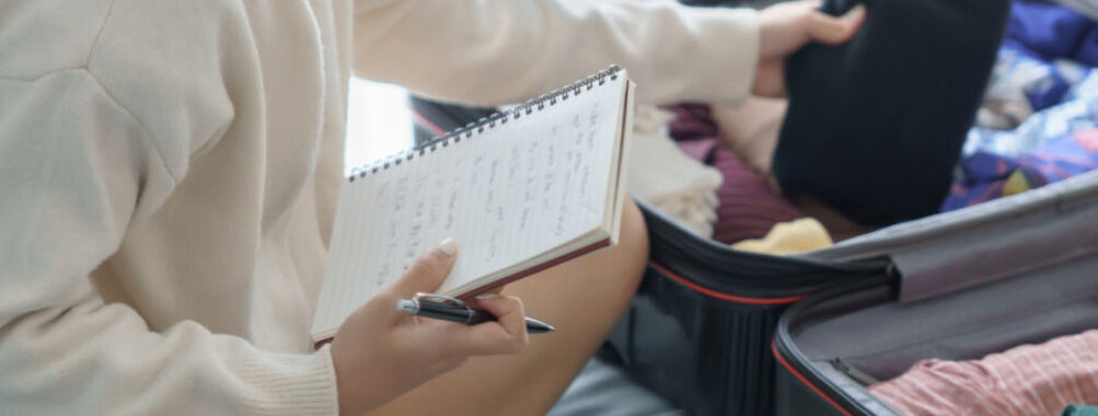 Woman in a bedroom organizing her vacation plans, focused on a travel checklist.
