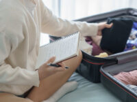 Woman in a bedroom organizing her vacation plans, focused on a travel checklist.