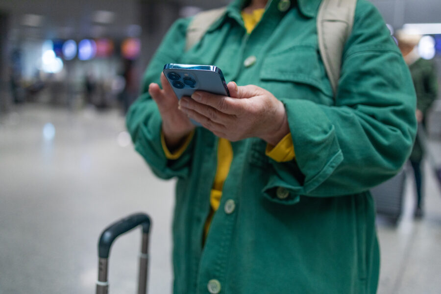 At the airport, a woman wearing a casual outfit, holds a smartphone as she embarks on a solo trip.