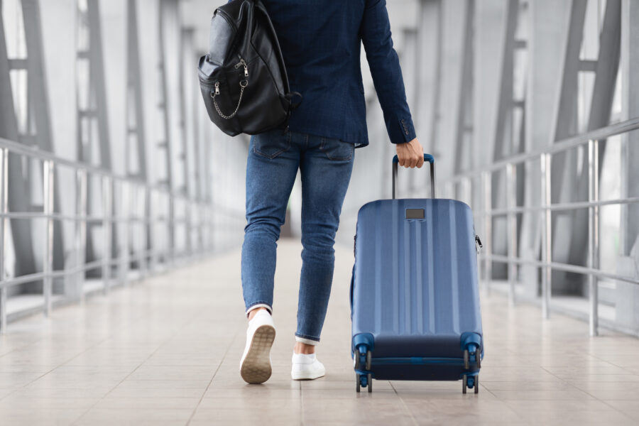 Rear view of an individual carrying a suitcase and bag while walking through a platform.