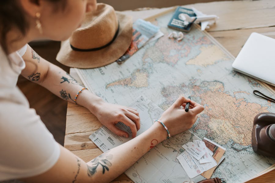 Traveler planning trip with map, sun hat, tickets, and laptop in cozy workspace.