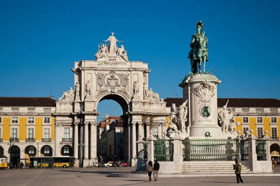 Triumphal arch and equestrian statue in sunlit European city plaza.