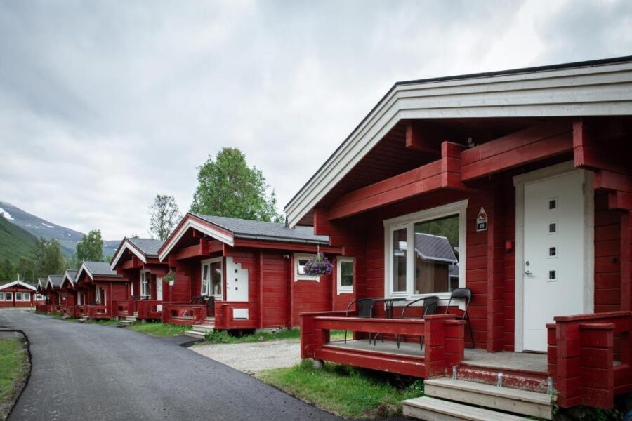 Scenic view of red cabins at Tromsø Lodge & Camping, set against a backdrop of majestic mountains and clear blue skies.
