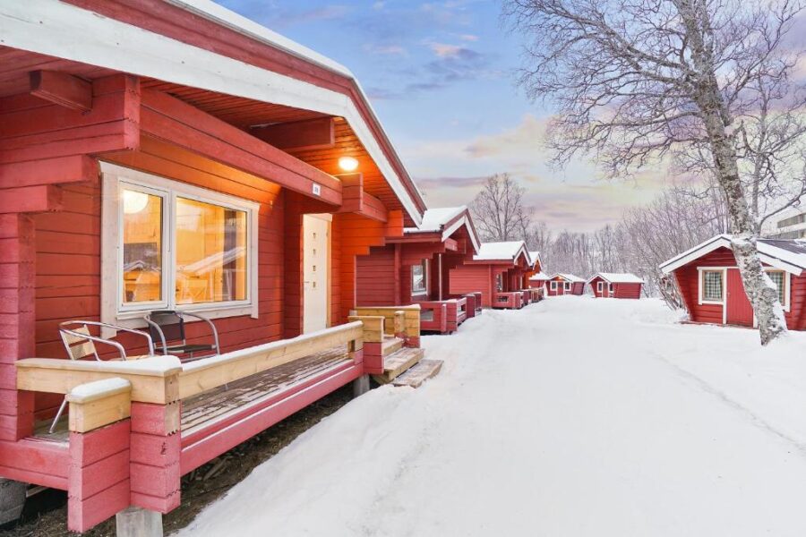 Snow-covered red cabins lined up at Tromsø Lodge & Camping, set against a serene winter backdrop.
