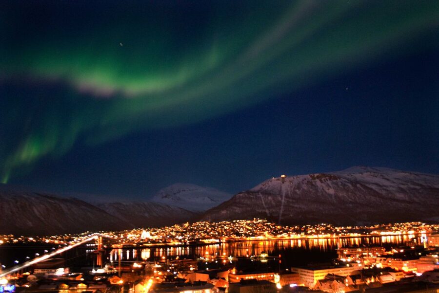 The aurora borealis illuminates the night sky above Tromsø, casting vibrant colors over the cityscape below.

