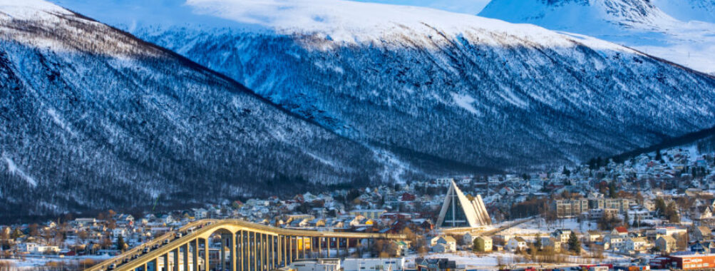 Aerial view of Tromso, Norway, showcasing colorful buildings, mountains, and the surrounding fjord under a clear sky.