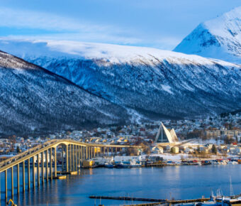Aerial view of Tromso, Norway, showcasing colorful buildings, mountains, and the surrounding fjord under a clear sky.