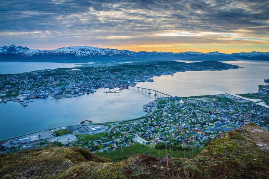Sunset casts vibrant colors over the city of Tromsø, Norway, highlighting its buildings and surrounding mountains.