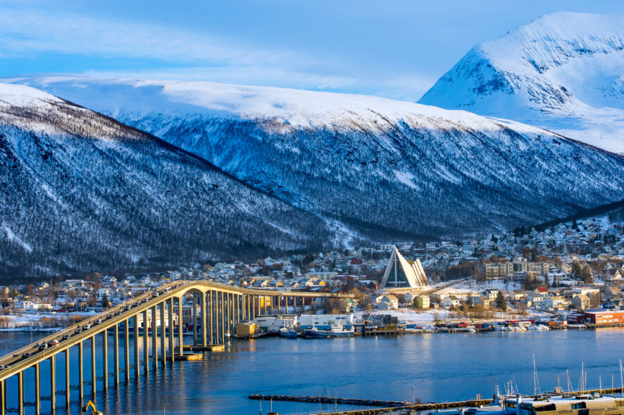 Aerial view of Tromso, Norway, showcasing colorful buildings, mountains, and the surrounding fjord under a clear sky.