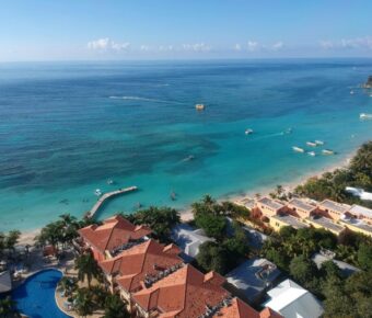 Aerial view of tropical beach, turquoise waters, palm trees, resort, and recreational activities.
