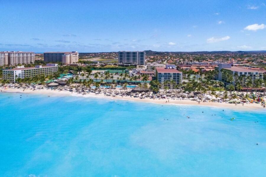 Tropical beach with turquoise sea, luxury resorts, palm trees, and lively vacationers enjoying paradise.
