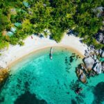 Aerial view of a tropical beach with palm trees, turquoise waters, and a small anchored boat.