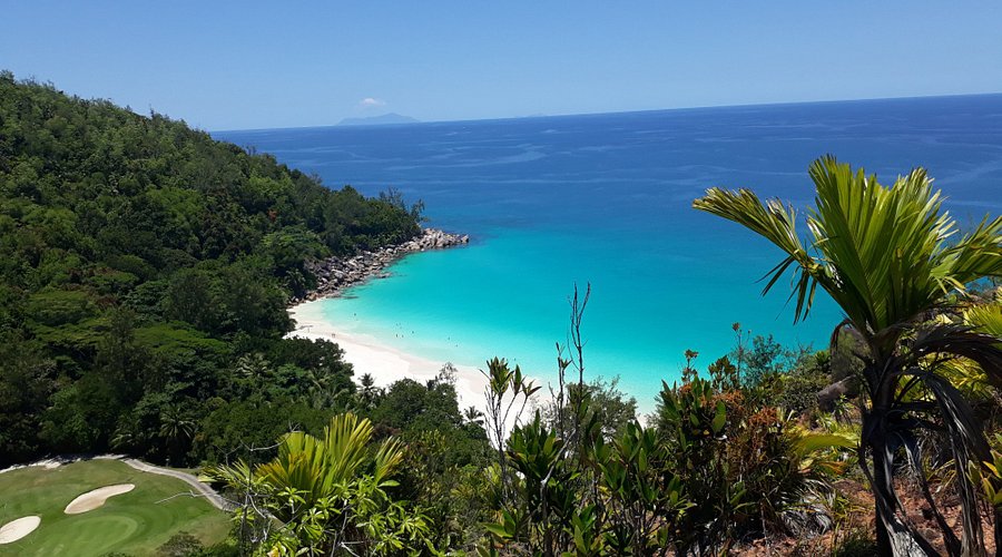 Tropical Seychelles beach with turquoise water, white sand cove, lush jungle cliffs and golf course.