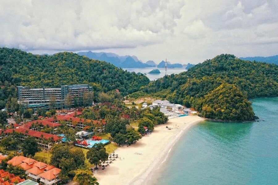 Aerial view of a lush tropical beach with resort, golden sands, and tranquil blue waters.