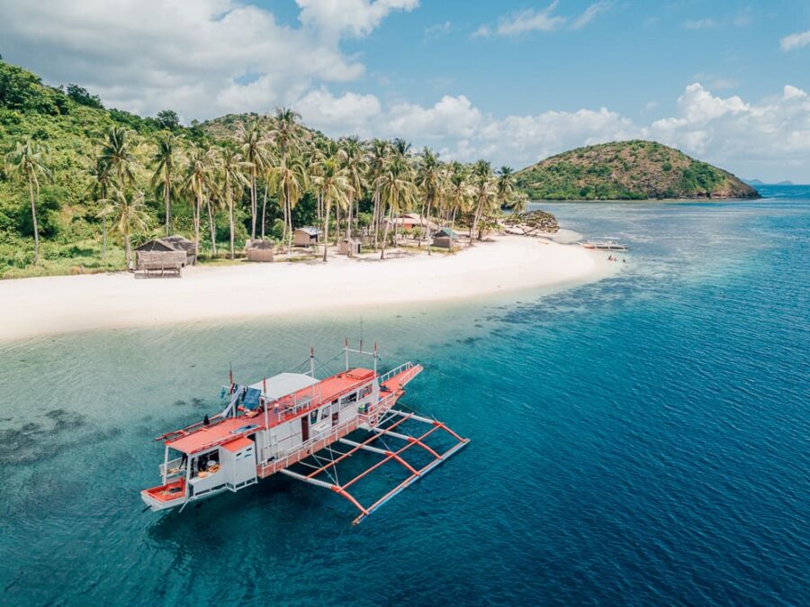 Tropical El Nido to Coron island with white-sand beach, palm trees and red-white outrigger boat.