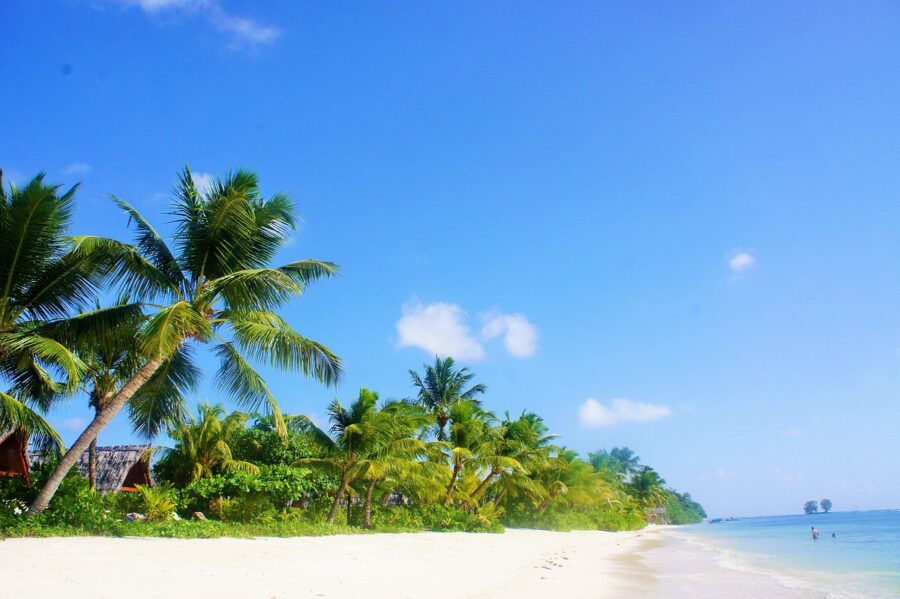 Idyllic tropical beach with white sand, palm trees, turquoise ocean and clear blue sky.