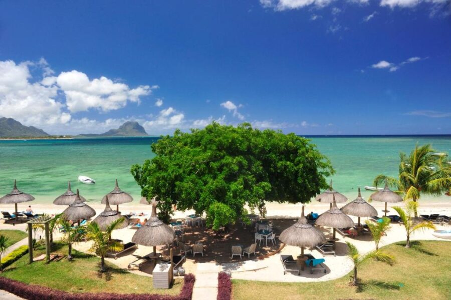 Luxury Mauritius beach resort with palm trees, loungers, turquoise lagoon, and mountain view.