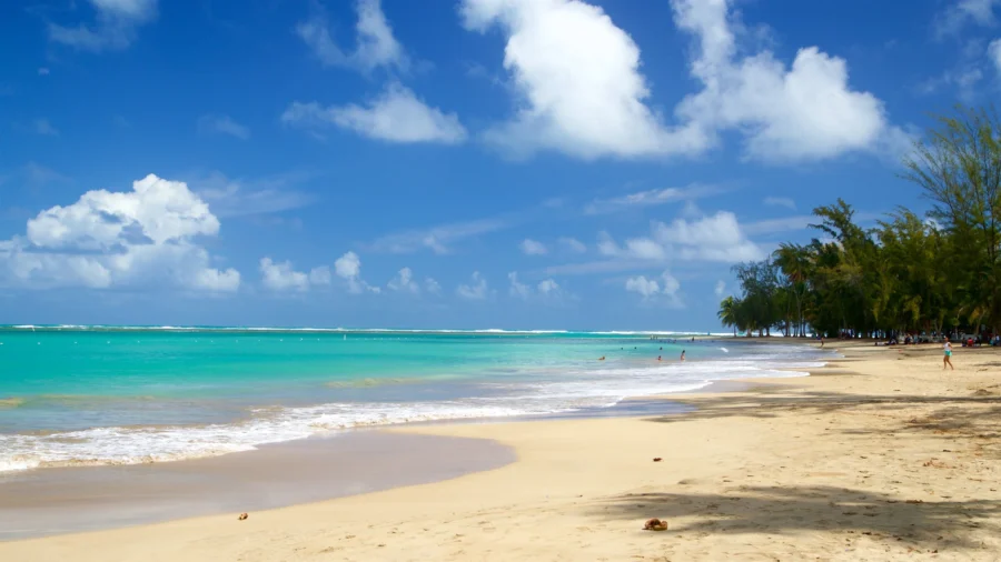 Tropical Luquillo Beach shoreline with turquoise ocean, palm trees, white sand, blue sky, relaxing vacation.