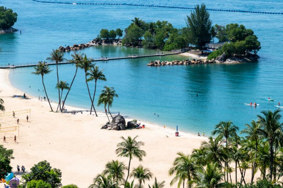 Idyllic tropical Sentosa Island with palm trees, lagoon, volleyball, boats, and vibrant activity.
