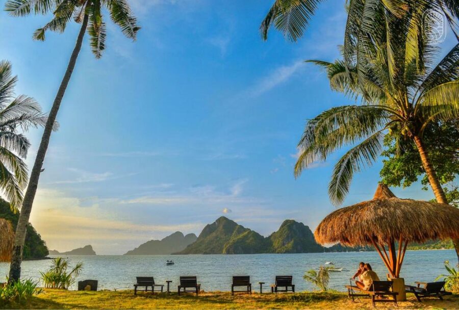 Tropical beach with palm trees, lounge chairs, palapa, calm water and island sunset.