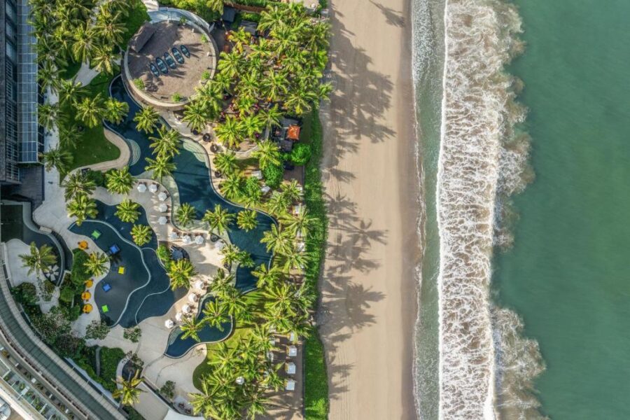 Aerial view of luxury Bali beachfront resort with tropical pool, palm trees, and turquoise ocean.