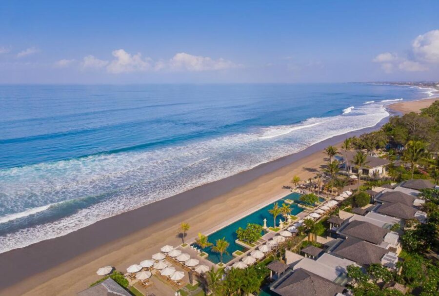 Aerial view of tropical beachfront resort with infinity pool, palm trees, sandy beach and turquoise ocean.