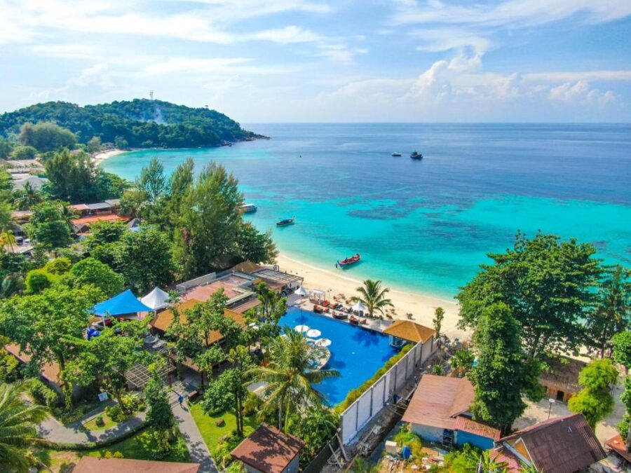 Aerial view of tropical beachfront resort with pool, palm trees, sandy beach and turquoise ocean.