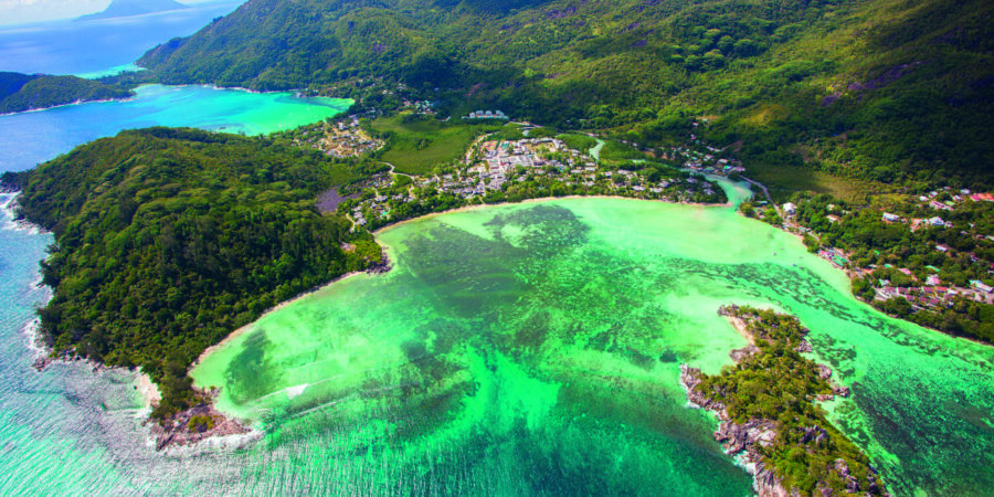 Aerial view of tropical lagoon village with turquoise water, lush green hills, and coastal bay.