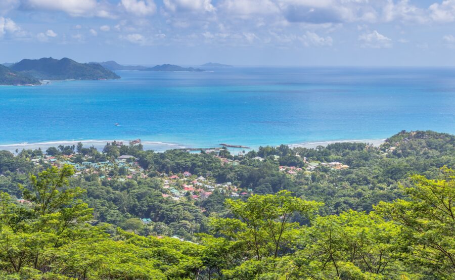 Tropical coastal village overlook with lush green hillside, sandy beach, turquoise ocean and distant islands.