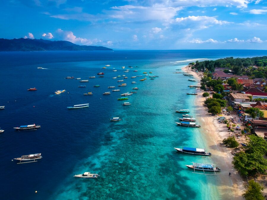 Aerial view of Gili Trawangan tropical beach, turquoise ocean, boats, coral reef, and coastal village.