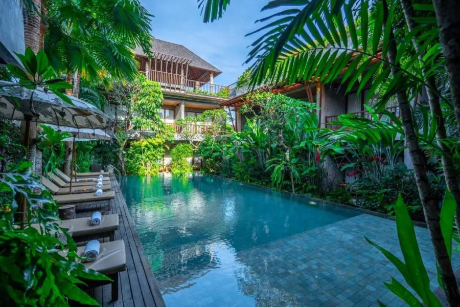 Luxury tropical courtyard pool retreat with lush jungle plants, wooden deck loungers, and villa.