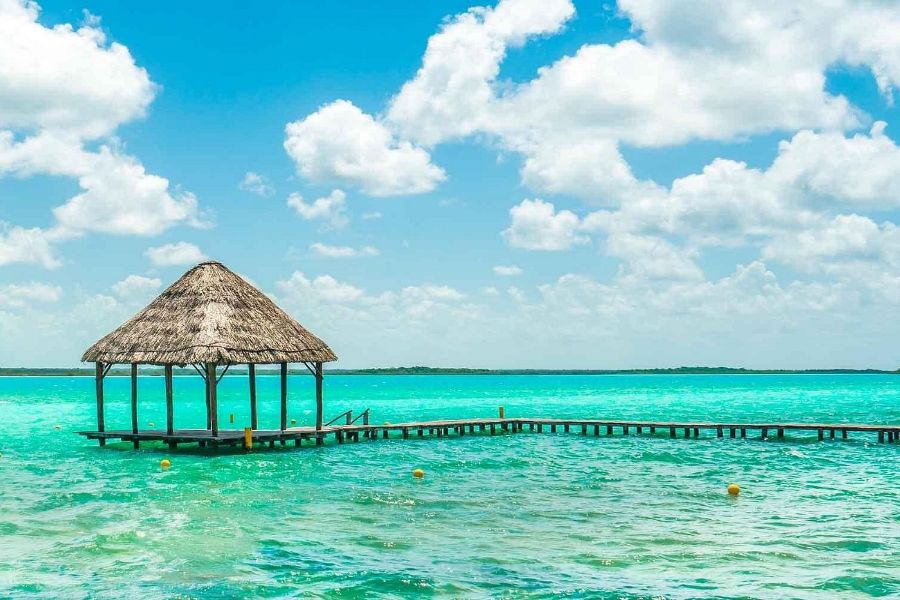Turquoise lagoon with wooden dock and gazebo under a clear sky.