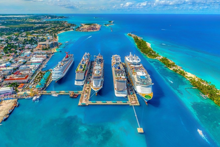 Aerial view of bustling tropical cruise port with ships, clear waters, and lush coastline.