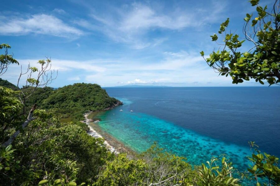 Aerial view of Apo Island tropical headland, turquoise reef waters and anchored boats.